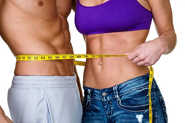 Casual woman measuring muscular mans waist for weight loss concept